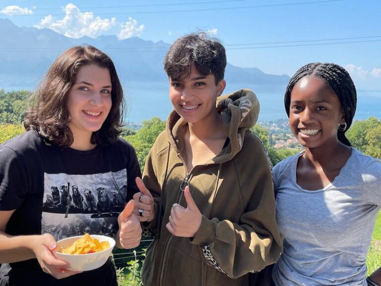 Three smiling students overlooking Lake Geneva