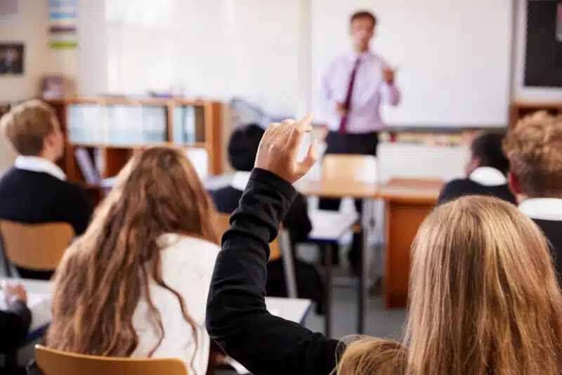 Élèves en uniforme levant la main en classe devant leur enseignant